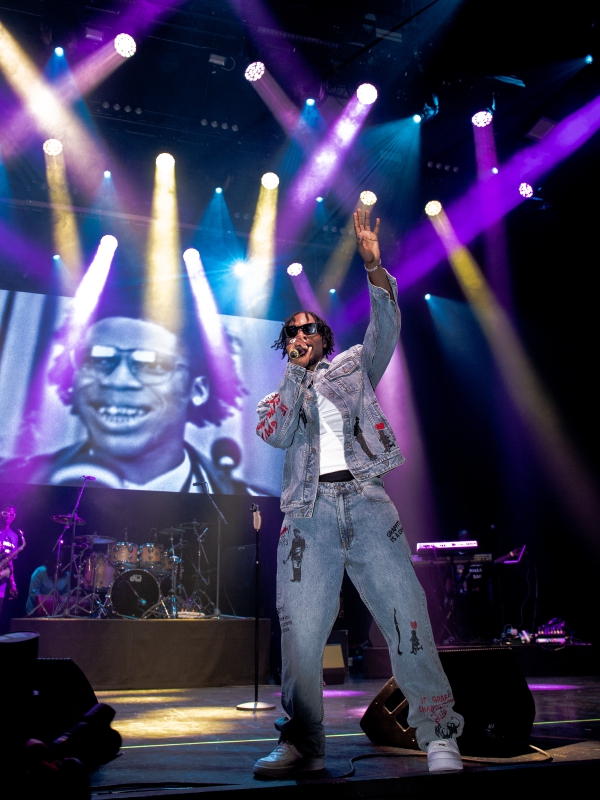L.A.X in a denim jacket and jeans performing on a vibrant stage with purple and blue lighting. — concert photography London by Lamss Media